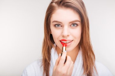 Attractive happy woman applying red lipstick on part of lip
