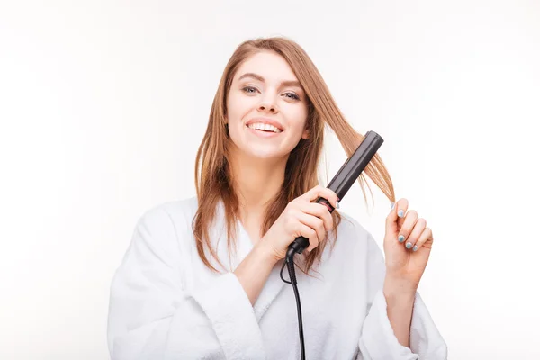 Jovem atraente alegre alisando seu cabelo com alisador — Fotografia de Stock