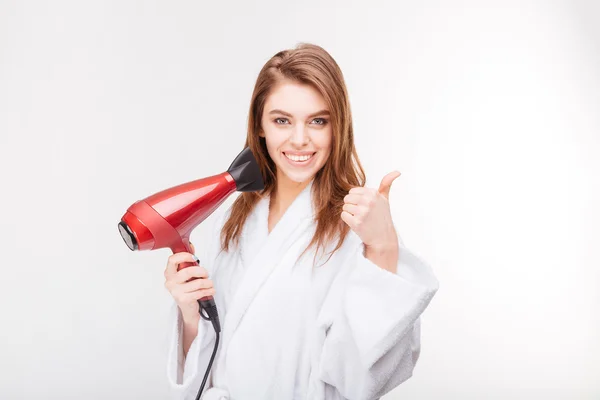 Mujer alegre sosteniendo secador de pelo y mostrando los pulgares hacia arriba —  Fotos de Stock