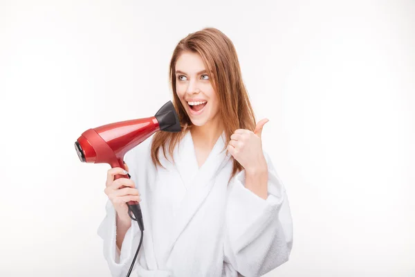 Jovem encantadora feliz com secador de cabelo mostrando polegares para cima — Fotografia de Stock