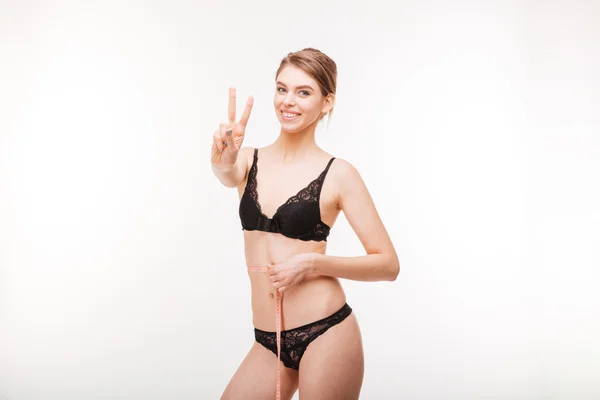 Cheerful woman showing victory sign and measuring her waist — Stock fotografie