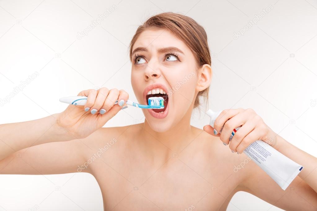 Pretty young woman using toothpaste and brushing her teeth