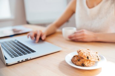 Businesswoman using laptop and drinking coffee with cookies on workplace