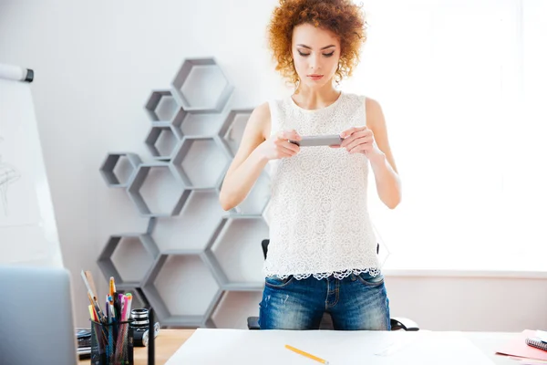 Concentrated woman taking photos of her workplace using smartphone — Stock Fotó