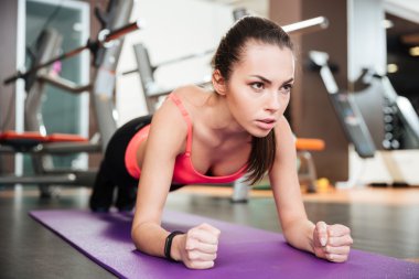 Concentrated beautiful young sportswoman doing plank exercise clipart