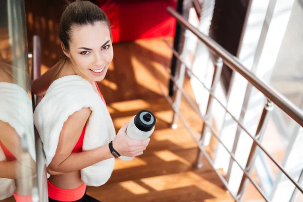 Schöne Sportlerin mit weißem Handtuch trinkt Wasser im Fitnessstudio — Stockfoto