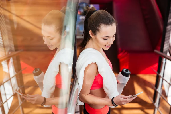 Lächelnde Sportlerin trinkt Wasser und nutzt Smartphone im Fitnessstudio — Stockfoto