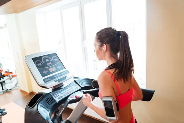 Beautiful woman athlete listening to music and running on treadmill — Stock Photo, Image