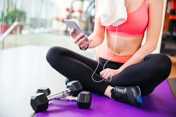 Vrouw atleet zitten en het gebruik van mobiele telefoon in sportschool — Stockfoto