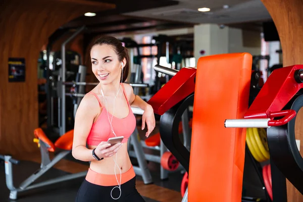 Deportista alegre escuchando música desde el teléfono móvil en el gimnasio — Foto de Stock