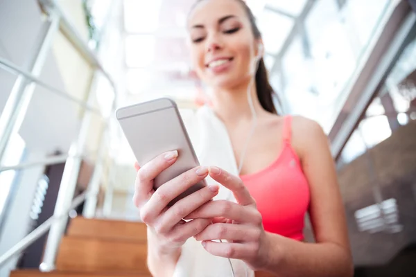 Glimlachend Sportvrouw zitten en het gebruik van mobiele telefoon in sportschool — Stockfoto