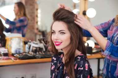 hairdresser making hairstyle to cheerful woman with long hair