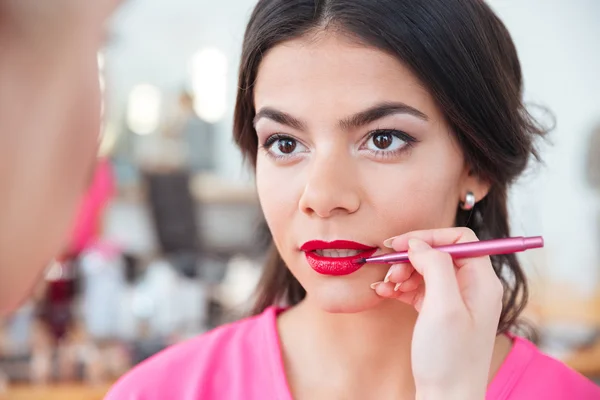 Young female visagiste applying red lipstick to lips of woman — Stock Photo, Image