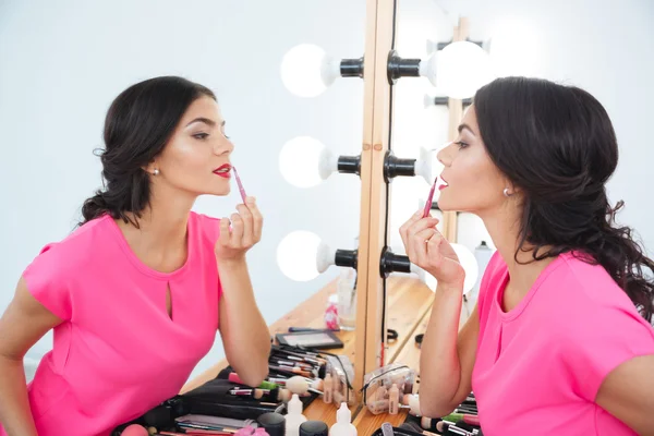 Schöne Frau, die neben Spiegel steht und roten Lippenstift aufsetzt — Stockfoto