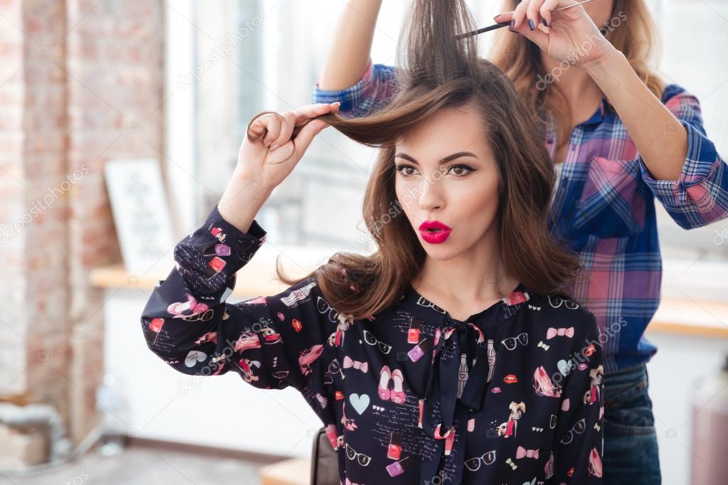 Woman hairdresser combing long hair of girl with red lipstick 