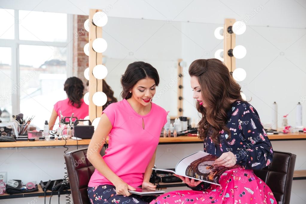 Two attractive young women using tablet and reading magazine