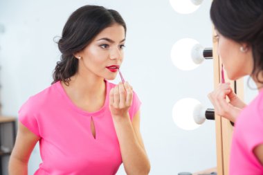 Aynaya bakarak ve kırmızı ruj tolips uygulayarak çekici kadın