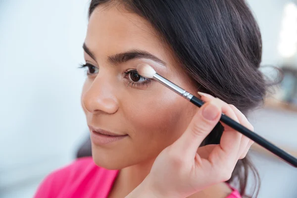 Maquillaje artista aplicando sombra de ojos a mujer atractiva — Foto de Stock