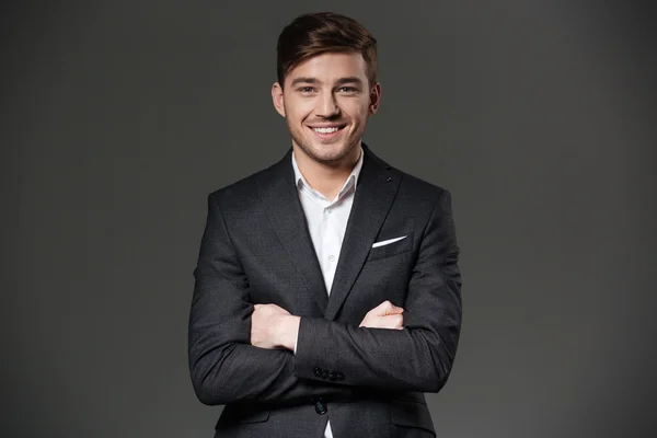 Smiling attractive businessman in black suit standing with hands folded — Stock Photo, Image