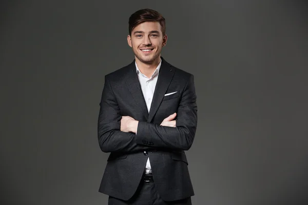 Cheerful successful young businessman standing with arms crossed — Stock Photo, Image