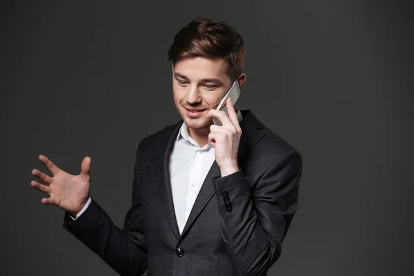 Smiling handsome young businessman gesturing and talking on cell phone — Stock Photo, Image