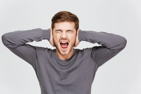 Depressiver aufgebrachter junger Mann verdeckte Ohren mit der Hand und schrie — Stockfoto