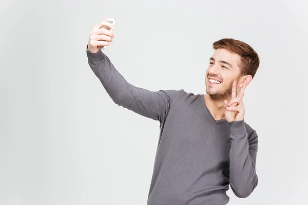 Sonriente hombre tomando selfie con smartphone y mostrando señal de paz — Foto de Stock