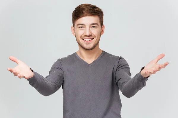 Joven guapo alegre sonriendo y mostrando gesto de bienvenida — Foto de Stock