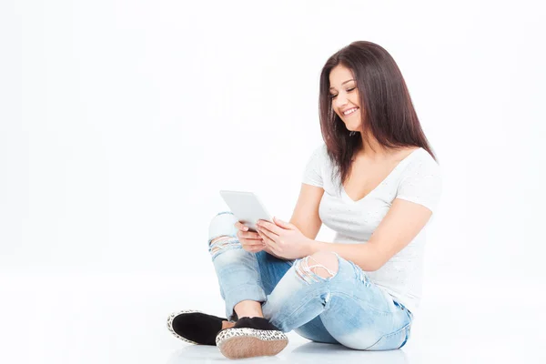Katta oturan ve tablet bilgisayar kullanarak gülümseyen kadın — Stok fotoğraf