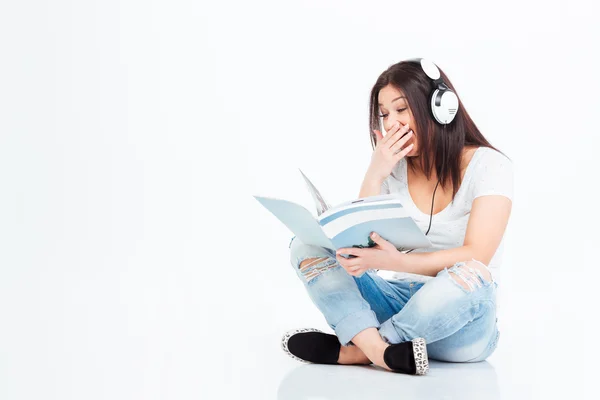 Woman sitting on the floor in headset and reading magazine — Stock Photo, Image