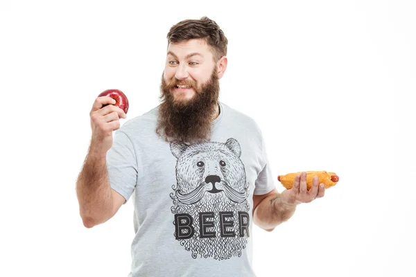 Веселый красивый мужчина с бородой держит яблоко и хот-дог — стоковое фото