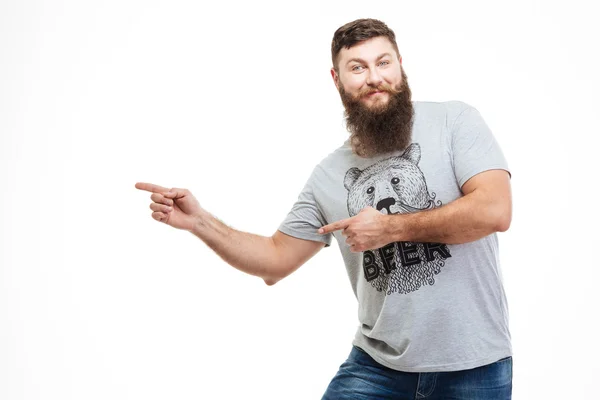 Homem atraente alegre com barba de pé e apontando para longe — Fotografia de Stock