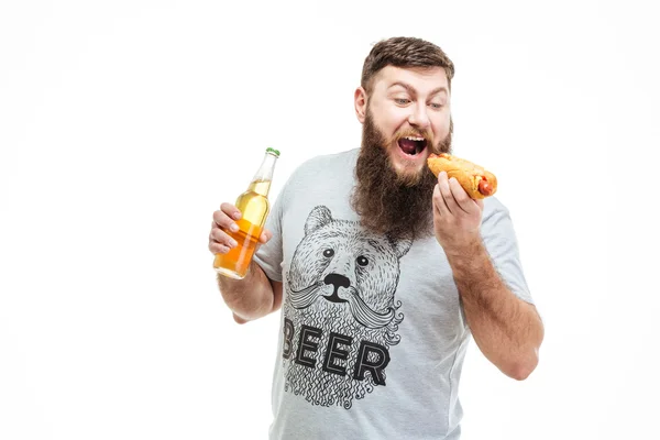 Homem barbudo segurando garrafa de cerveja e comendo cachorro quente — Fotografia de Stock