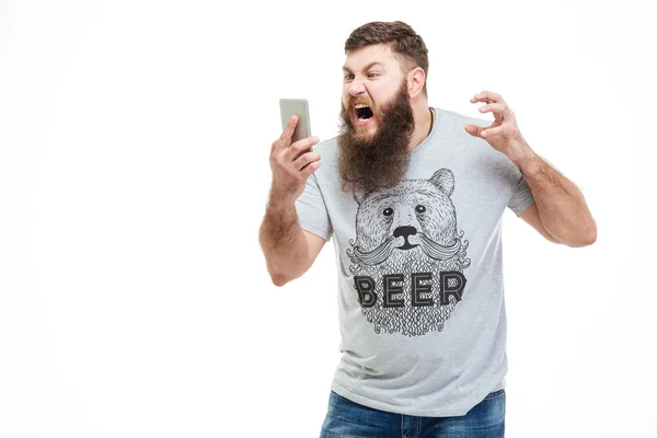 Irritated angry man with beard holding smartphone and shouting — Stock Photo, Image