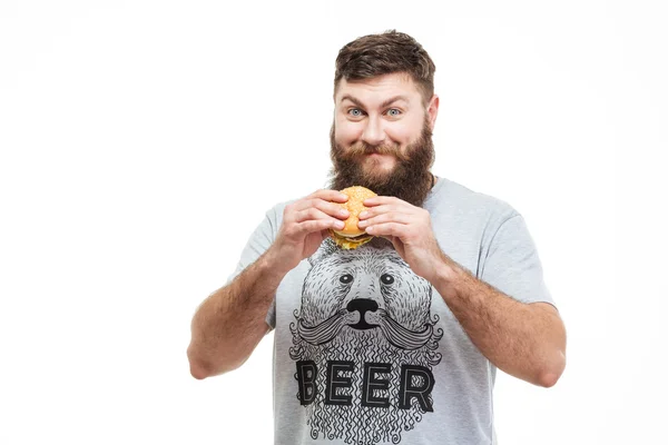 Sorrindo homem bonito com barba de pé e segurando hambúrguer — Fotografia de Stock
