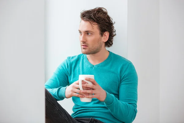 Pencere kenarında oturan ve kahve içme düşünceli genç adam — Stok fotoğraf