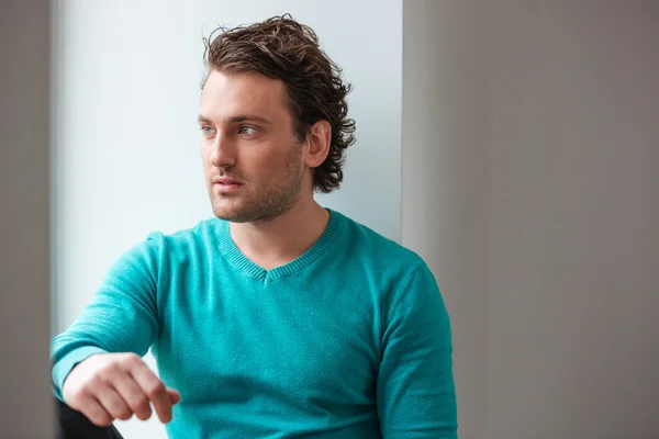 Handsome pensive young man sitting and looking at the window — Stock Photo, Image