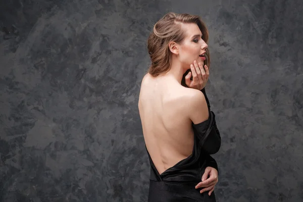 Alluring charming young woman in black dress with open back — Stock Photo, Image