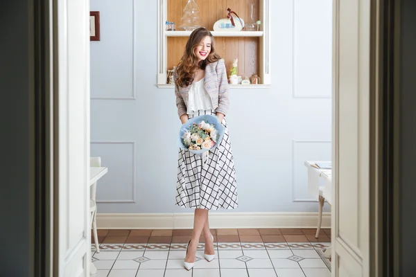 Cheerful woman standing in cafe and holding bouquet of flowers — Stock Photo, Image