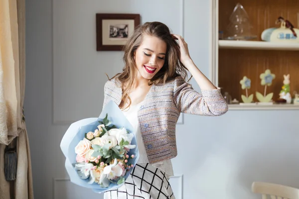 Mulher feliz com buquê de flores de pé perto da janela — Fotografia de Stock