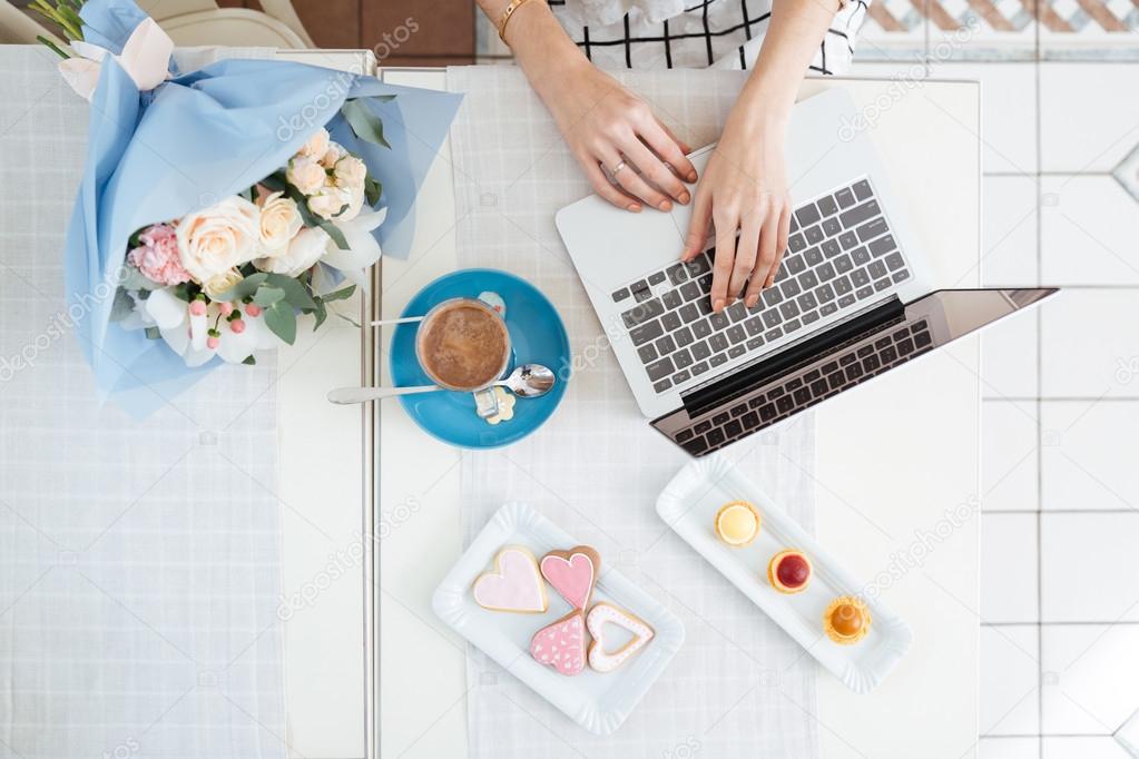 Hands of young woman using laptop at table in cafe