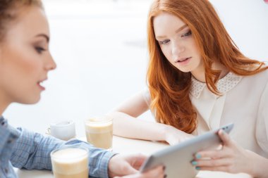Konuşmak ve kullanarak iki konsantre kadın cafede birlikte tablet