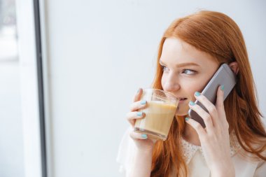 Kadın içme kahve gülümseyen ve cep telefonuyla konuşuyor