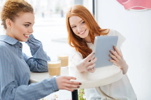 Dvě usmívající se ženy při pohledu na obrazovku tabletu v kavárně — Stock fotografie