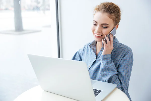 Mulher feliz falando no telefone celular e usando laptop — Fotografia de Stock