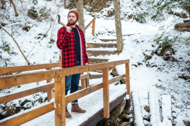 Kışın ahşap köprü üzerinde balta duran sakallı adam 