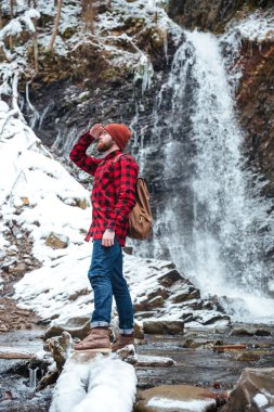 Dağlar, şelale yakınındaki kışın yürüyen yakışıklı berded adam