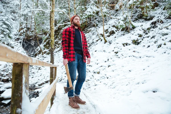 Hermoso leñador barbudo sosteniendo hacha en el bosque de invierno de montaña — Foto de Stock