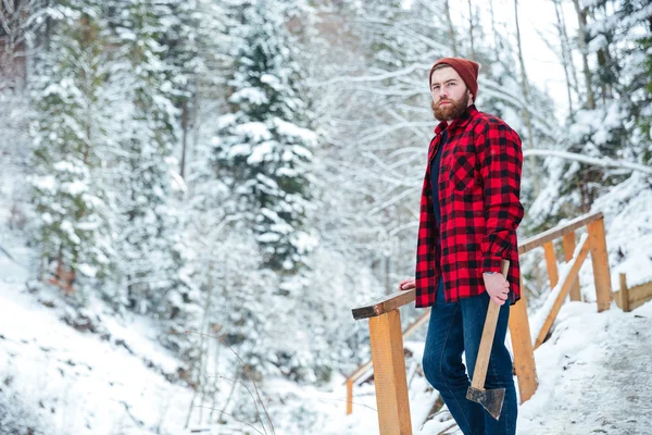 Красивый задумчивый человек с топором, стоящий в горном зимнем лесу — стоковое фото