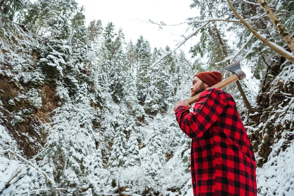 Hombre barbudo con hacha caminando en el bosque de invierno de montaña — Foto de Stock